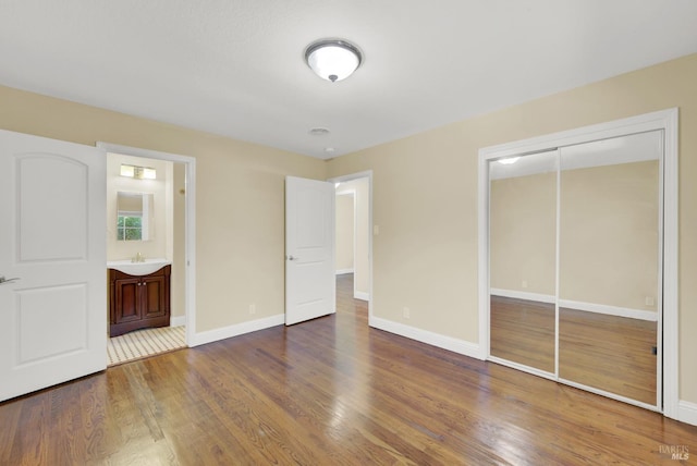 unfurnished bedroom with wood finished floors, a sink, a closet, and baseboards