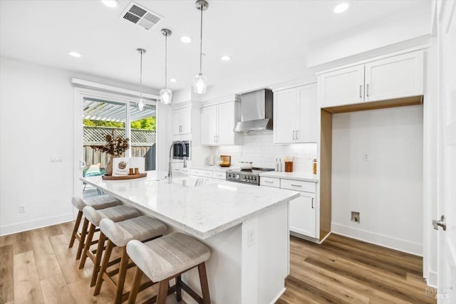 kitchen with wall chimney exhaust hood, visible vents, appliances with stainless steel finishes, a sink, and backsplash