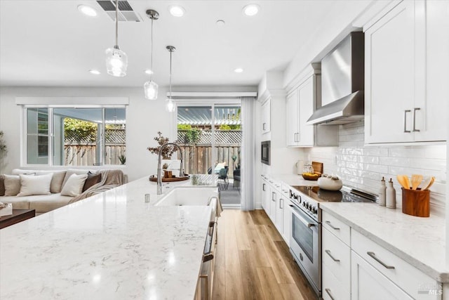 kitchen featuring high end stainless steel range, decorative backsplash, wall chimney exhaust hood, and a healthy amount of sunlight