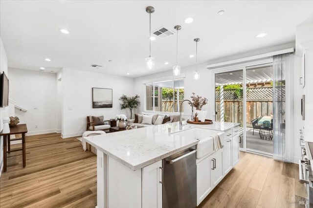 kitchen featuring light wood finished floors, dishwasher, a sink, and a center island with sink