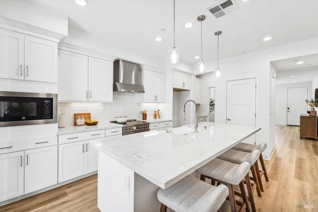 kitchen with wall chimney range hood, white cabinets, visible vents, stainless steel range, and built in microwave