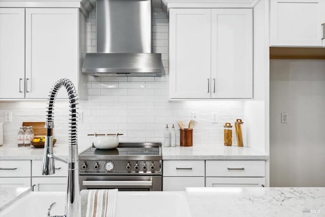 kitchen with high end stainless steel range oven, decorative backsplash, wall chimney range hood, and white cabinetry