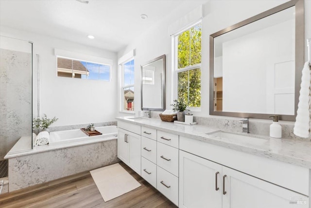 bathroom with double vanity, a bath, a sink, and wood finished floors