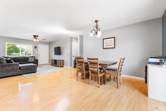 dining room featuring light wood-type flooring, ceiling fan with notable chandelier, and baseboards