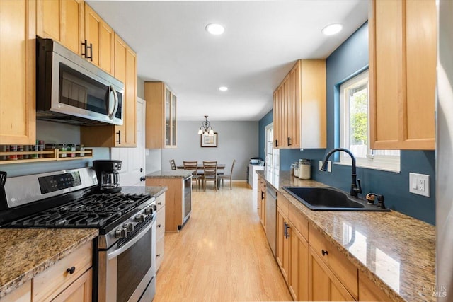 kitchen with light wood-style flooring, appliances with stainless steel finishes, a sink, and light stone countertops