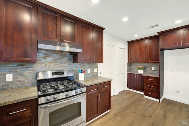 kitchen featuring light wood-style flooring, stainless steel gas range oven, under cabinet range hood, light stone countertops, and visible vents