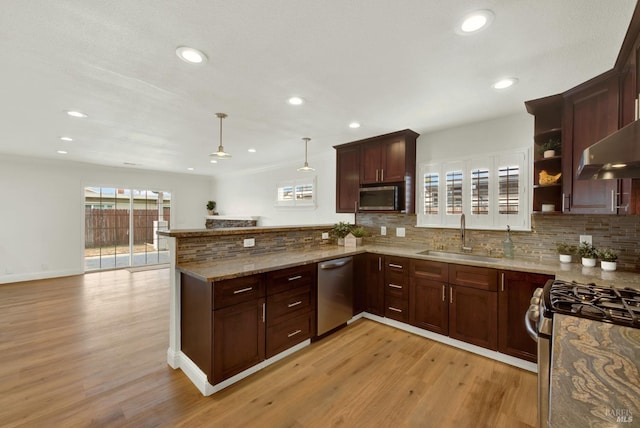 kitchen with a peninsula, backsplash, stainless steel appliances, light wood finished floors, and a sink