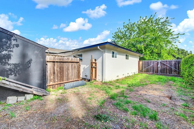 view of property exterior featuring crawl space, stucco siding, fence, and a gate