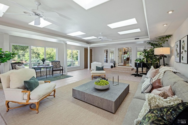 tiled living area featuring a raised ceiling, a skylight, and ceiling fan