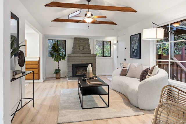 living area with light wood-style flooring, a fireplace, a ceiling fan, and vaulted ceiling with beams
