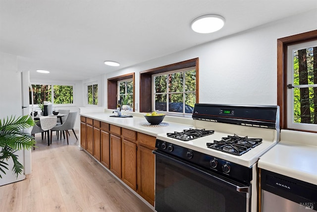 kitchen featuring a wealth of natural light, brown cabinetry, light countertops, range with gas stovetop, and light wood finished floors