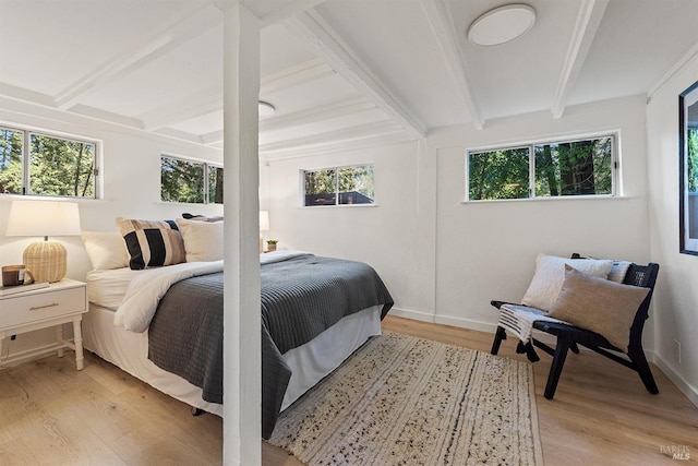 bedroom featuring baseboards, multiple windows, light wood-type flooring, and beamed ceiling