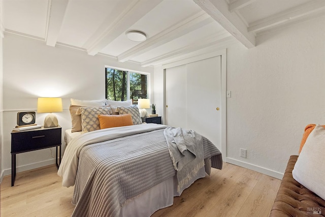 bedroom featuring beam ceiling, light wood-style flooring, a closet, and baseboards