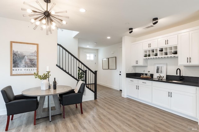 dining room featuring visible vents, a notable chandelier, light wood-type flooring, wet bar, and stairs