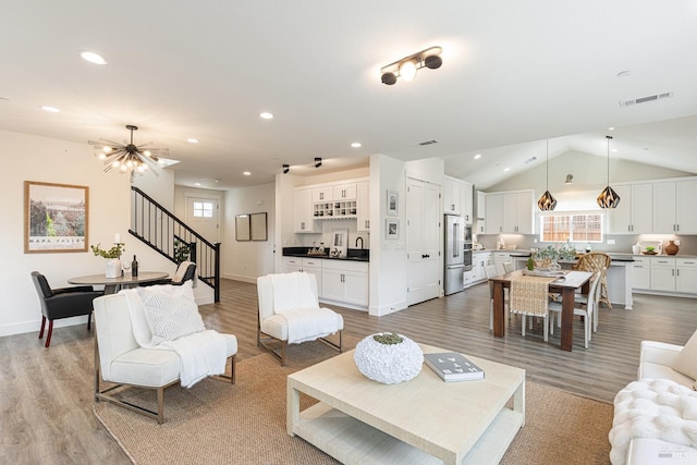 living area featuring visible vents, stairway, light wood-style floors, and lofted ceiling