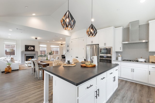 kitchen with wall chimney range hood, dark countertops, light wood-style floors, stainless steel appliances, and a kitchen island
