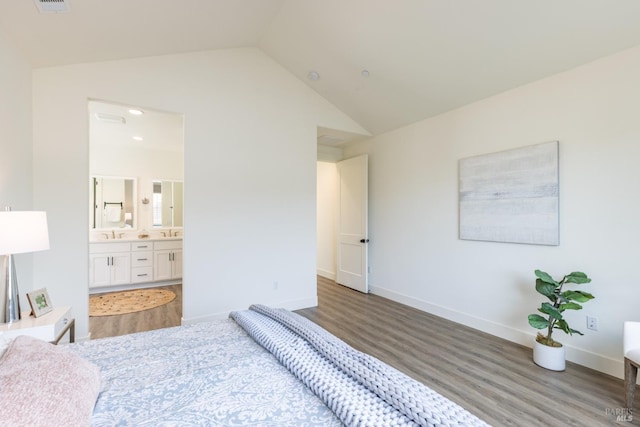 bedroom featuring baseboards, vaulted ceiling, ensuite bath, a sink, and wood finished floors