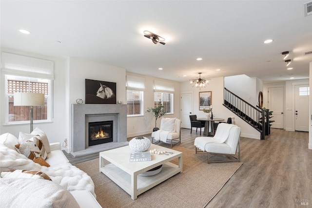 living area featuring a glass covered fireplace, recessed lighting, stairs, light wood-style floors, and visible vents