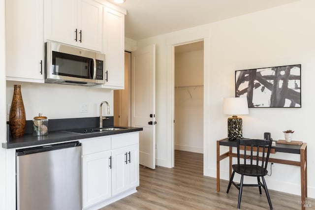 kitchen featuring dishwashing machine, light wood-style flooring, white cabinets, stainless steel microwave, and dark countertops