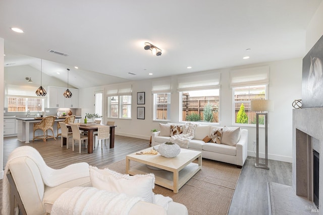 living room featuring a fireplace, vaulted ceiling, visible vents, recessed lighting, and light wood finished floors