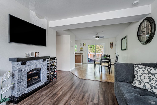 living room featuring a stone fireplace, ceiling fan, wood finished floors, and baseboards