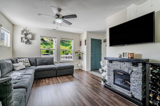 living room with visible vents, baseboards, a stone fireplace, ceiling fan, and dark wood-style floors