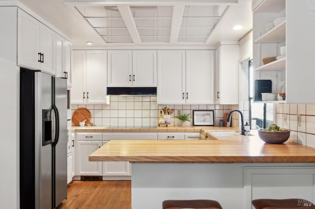 kitchen with a peninsula, stainless steel fridge with ice dispenser, a sink, and white cabinetry