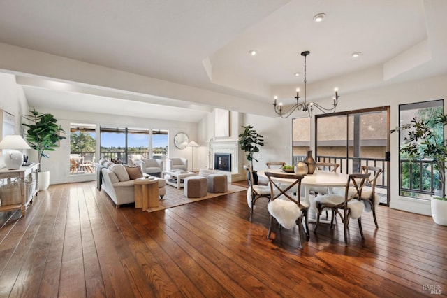 dining area with a notable chandelier, dark wood-style floors, a tray ceiling, recessed lighting, and a glass covered fireplace