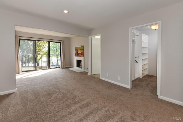 unfurnished living room featuring a lit fireplace, baseboards, carpet, and recessed lighting