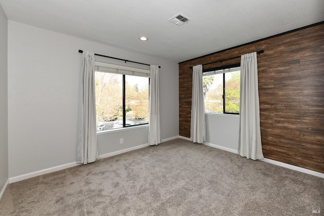 carpeted spare room with wood walls, baseboards, visible vents, and recessed lighting