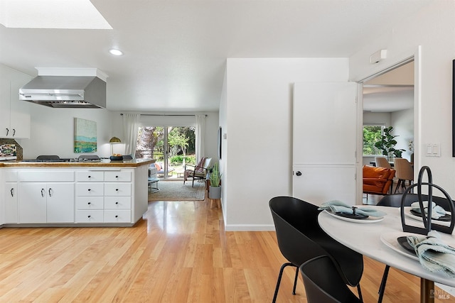 kitchen with wall chimney exhaust hood, a peninsula, white cabinetry, gas cooktop, and light wood finished floors