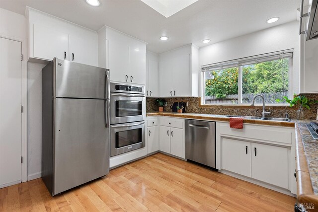 kitchen featuring a sink, decorative backsplash, appliances with stainless steel finishes, and light wood-style flooring