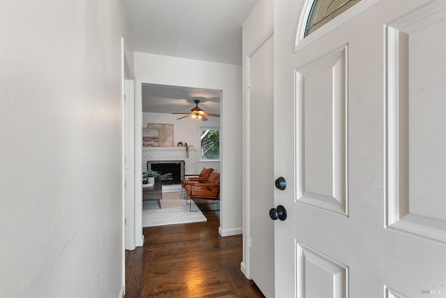 entrance foyer with dark wood-style flooring, a ceiling fan, and a brick fireplace