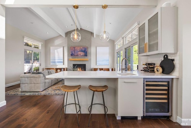 kitchen featuring a peninsula, dark wood-style flooring, a sink, vaulted ceiling with beams, and beverage cooler