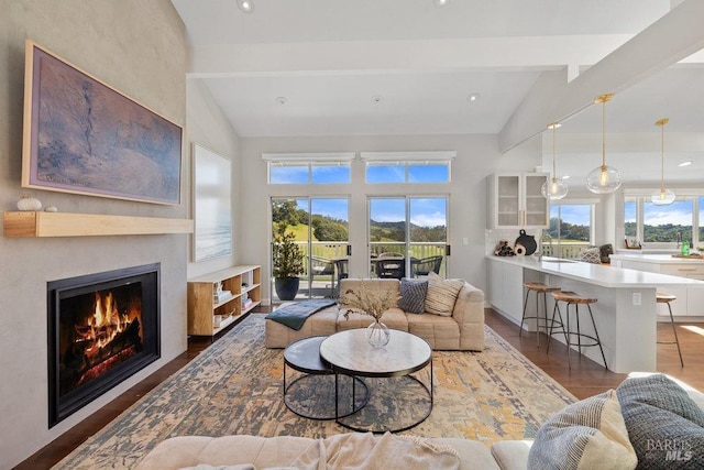 living area with vaulted ceiling with beams, a warm lit fireplace, and wood finished floors