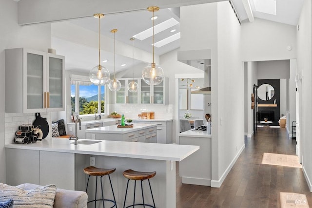 kitchen featuring wall chimney range hood, a peninsula, light countertops, a skylight, and a sink