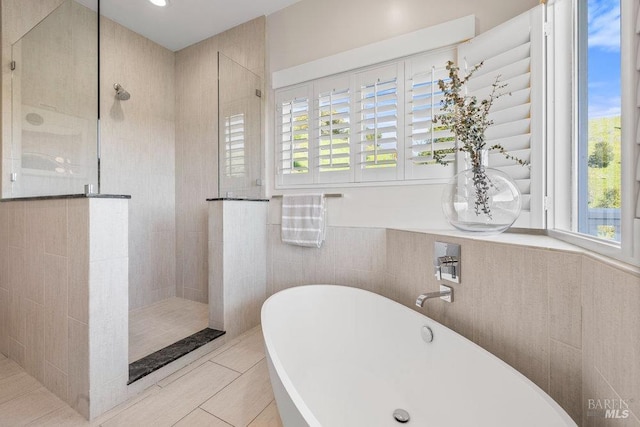 bathroom with tile walls, a freestanding bath, a walk in shower, and tile patterned floors