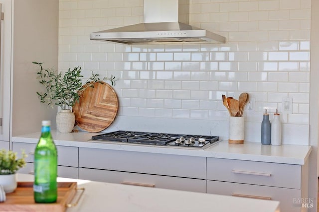 kitchen featuring stainless steel gas cooktop, light countertops, wall chimney range hood, and backsplash