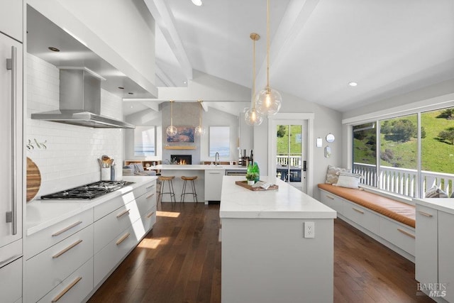 kitchen featuring wall chimney exhaust hood, a kitchen island, stainless steel gas cooktop, vaulted ceiling with beams, and dark wood-style floors