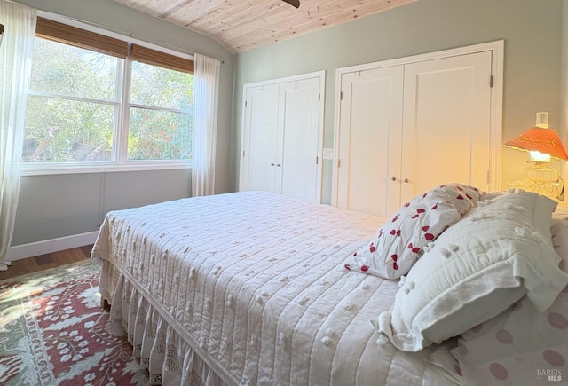 bedroom with vaulted ceiling, wood finished floors, wooden ceiling, baseboards, and two closets