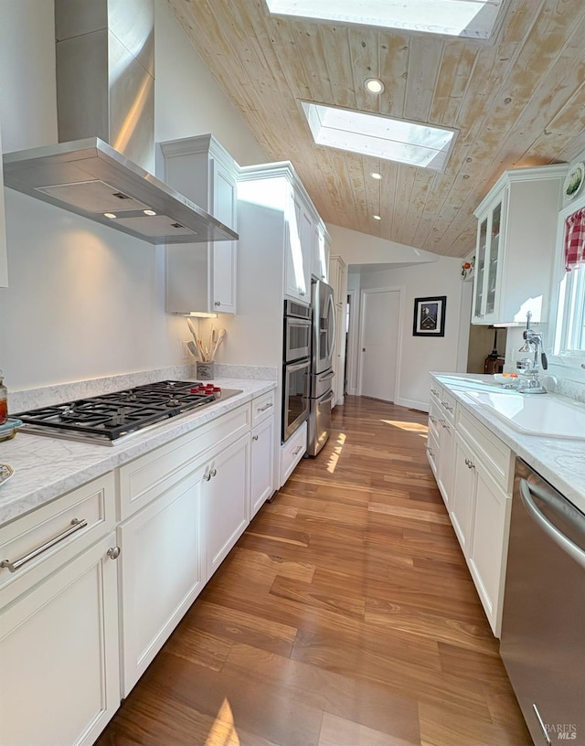 kitchen featuring stainless steel appliances, wall chimney range hood, wooden ceiling, a sink, and lofted ceiling with skylight