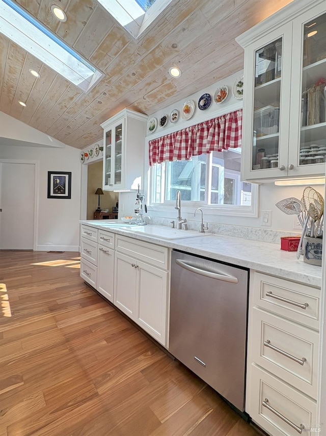 kitchen with stainless steel dishwasher, a sink, light wood-style floors, lofted ceiling with skylight, and wood ceiling