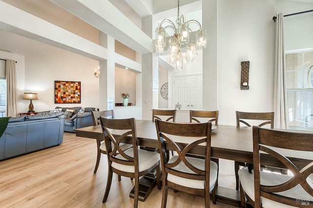 dining area with a high ceiling, light wood-type flooring, and an inviting chandelier