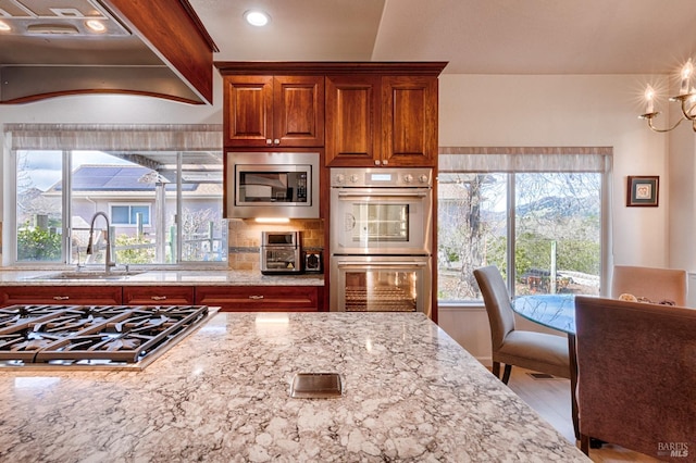 kitchen featuring a sink, brown cabinets, stainless steel appliances, decorative backsplash, and light stone counters