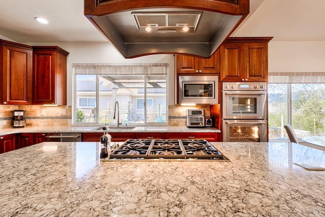 kitchen with appliances with stainless steel finishes, a sink, ventilation hood, and light stone counters