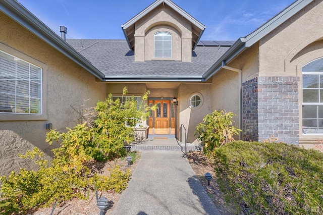 view of exterior entry featuring roof with shingles, stucco siding, and solar panels