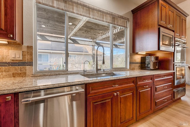 kitchen featuring a sink, light wood-style floors, stainless steel appliances, decorative backsplash, and light stone counters