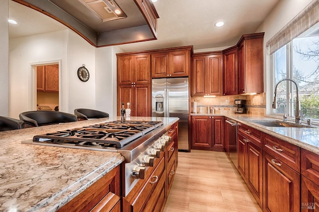 kitchen featuring tasteful backsplash, a sink, appliances with stainless steel finishes, light wood finished floors, and light stone countertops