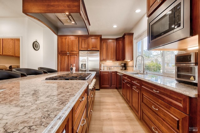 kitchen with a sink, appliances with stainless steel finishes, light stone counters, and light wood finished floors
