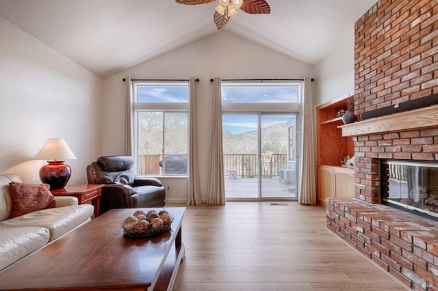 living area featuring a fireplace, light wood-type flooring, a ceiling fan, visible vents, and vaulted ceiling